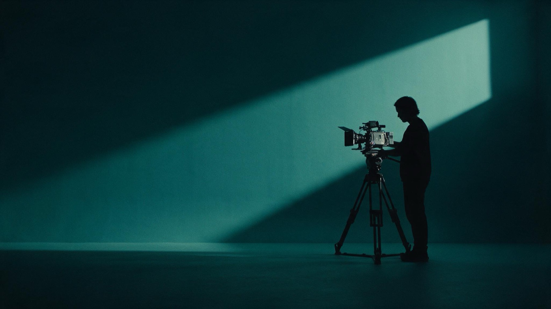 Cinematographer in silhouette adjusting a cinema camera against a deep-teal studio wall